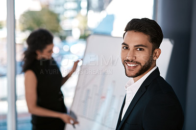 Buy stock photo Cropped portrait of a handsome young businessman standing while his colleague prepares a presentation on a white board behind him