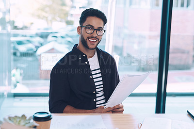 Buy stock photo Cropped portrait of a handsome young businessman sitting alone in his office and reading through paperwork