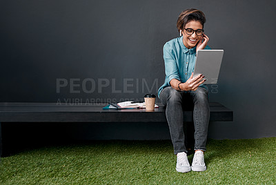 Buy stock photo Full length shot of an attractive young woman sitting alone on a bench outside and using a tablet