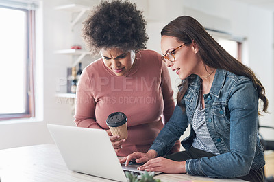 Buy stock photo Shot of two young businesswomen using a laptop in a modern office