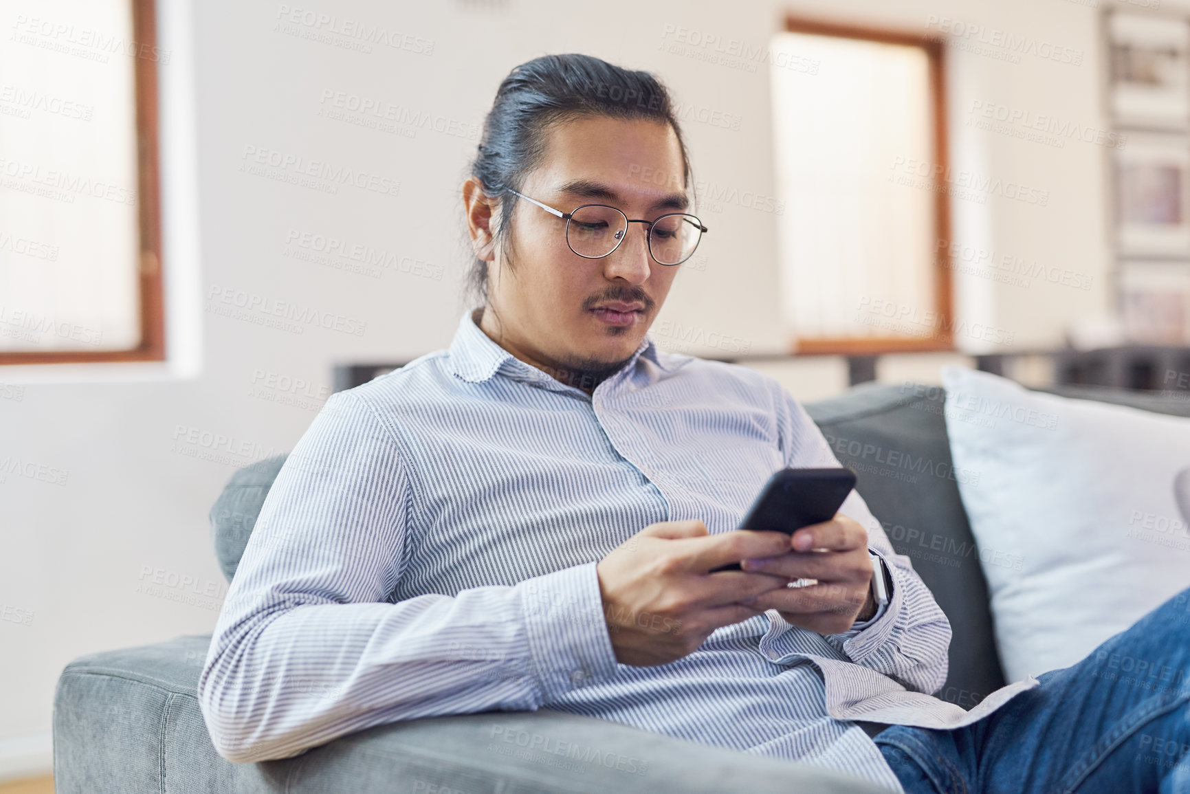 Buy stock photo Shot of a young businessman using a smartphone on a sofa in a modern office