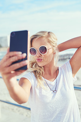 Buy stock photo Cropped shot of a young woman taking a selfie while spending the day by the sea