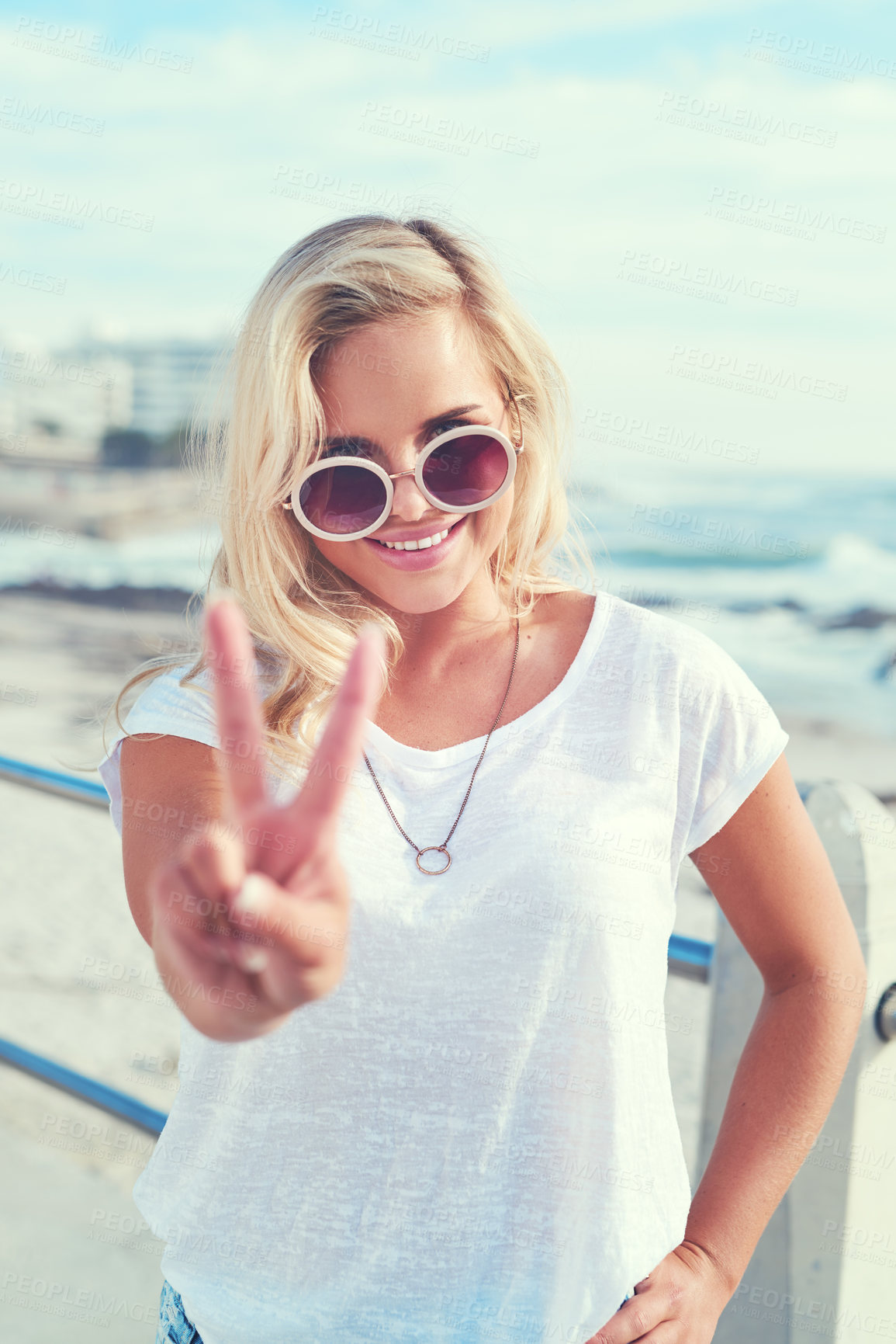 Buy stock photo Shot of a young woman showing the peace sign while standing outdoors on a sunny day