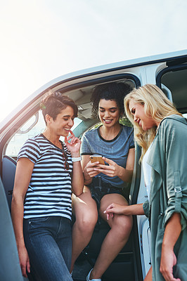 Buy stock photo Shot of friends looking at something on a cellphone while out on a road trip