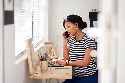 Buy stock photo Shot of an attractive young artist using a laptop and making a phone call inside her studio at hom