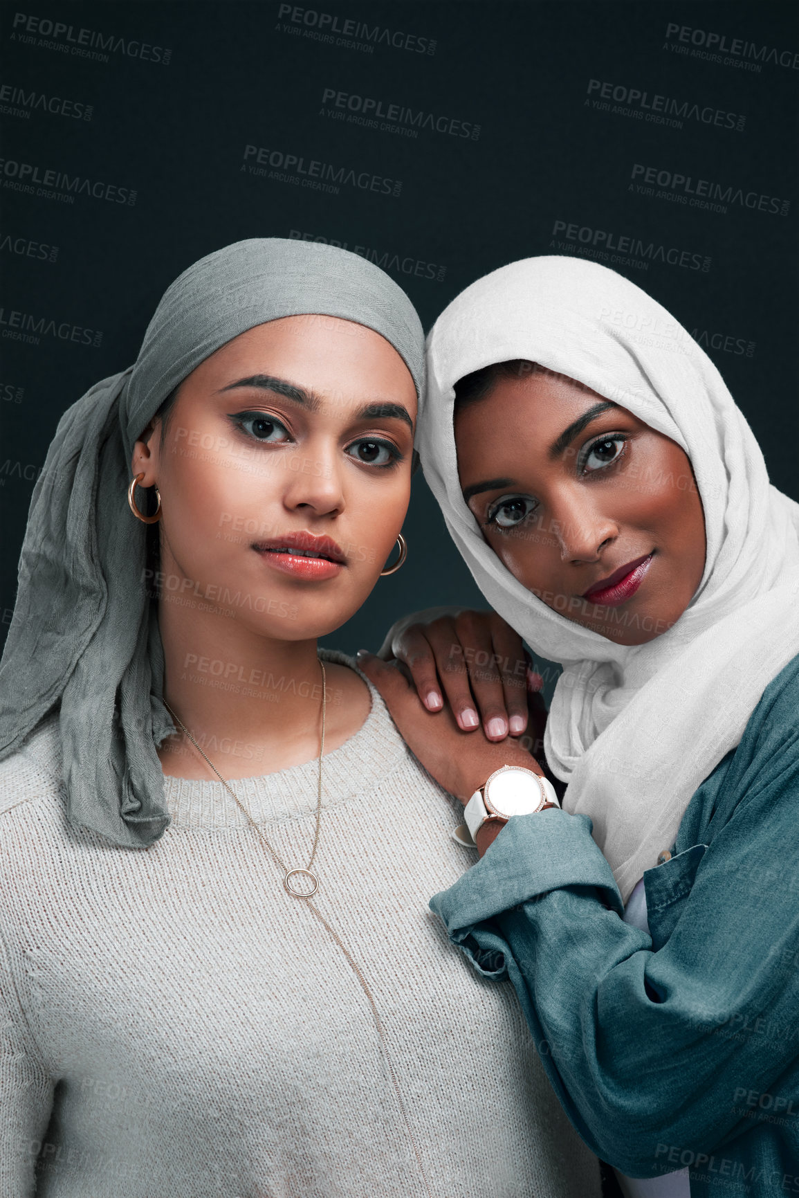 Buy stock photo Cropped shot of two attractive young women wearing hijabs and standing close together against a black background in the studio