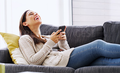 Buy stock photo Shot of an attractive young woman using her cellphone while relaxing on a couch at home