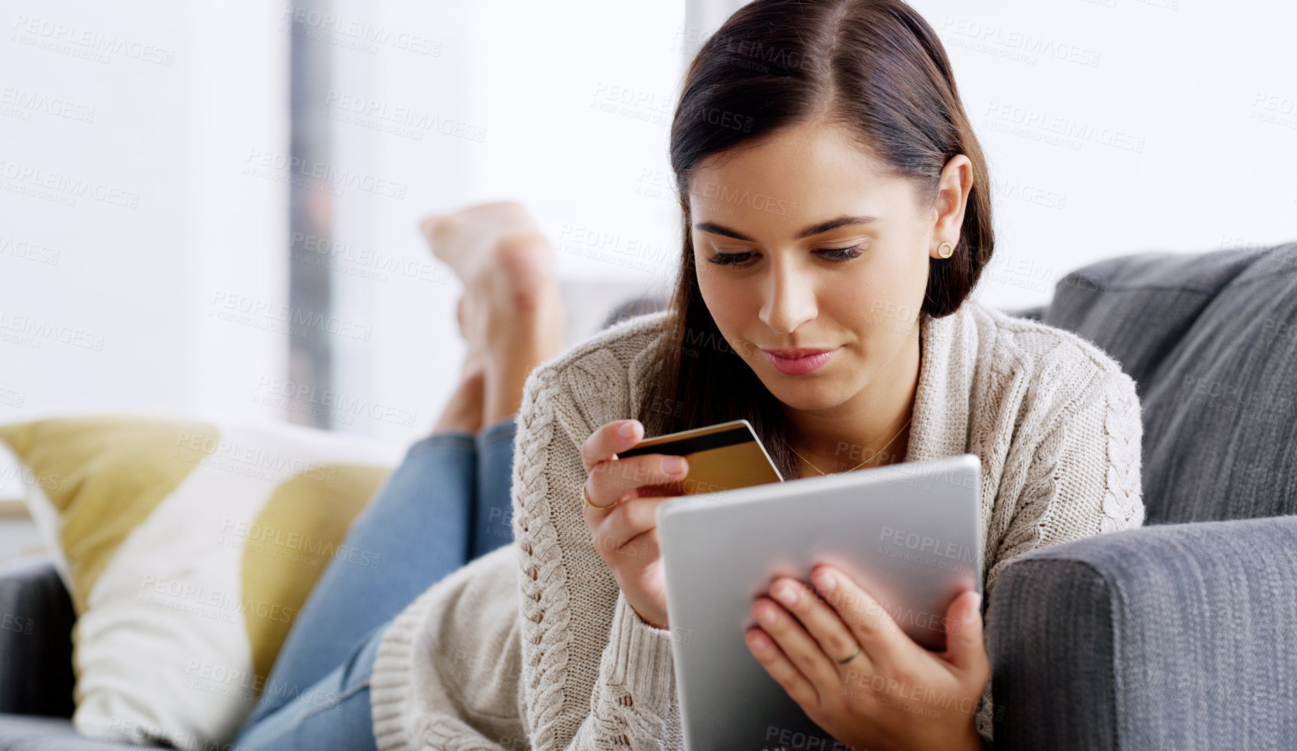 Buy stock photo Shot of an attractive young woman using her credit card and digital tablet while relaxing on a sofa at home