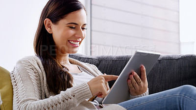 Buy stock photo Shot of an attractive young woman using a digital tablet while relaxing on a sofa at home