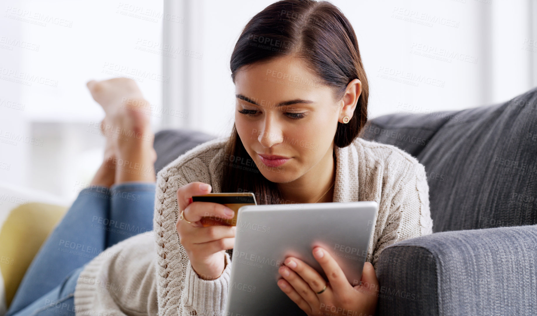 Buy stock photo Shot of an attractive young woman using her credit card and digital tablet while relaxing on a sofa at home