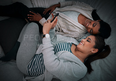 Buy stock photo Cropped shot of two young women looking at something on a cellphone while lying on a bed