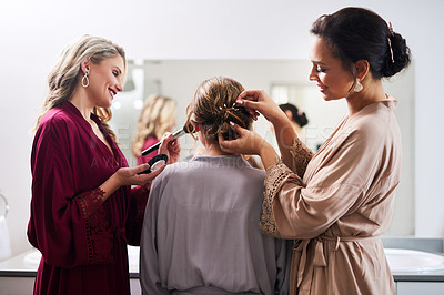 Buy stock photo Cropped shot of two attractive young bridesmaids doing the bride's hair and make-up in preparation of her wedding
