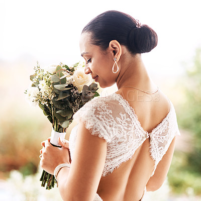 Buy stock photo Shot of a beautiful young bride smelling her bouquet of flowers outdoors on her wedding day