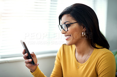Buy stock photo Cropped shot of an attractive young woman sitting alone and texting on her cellphone in her home