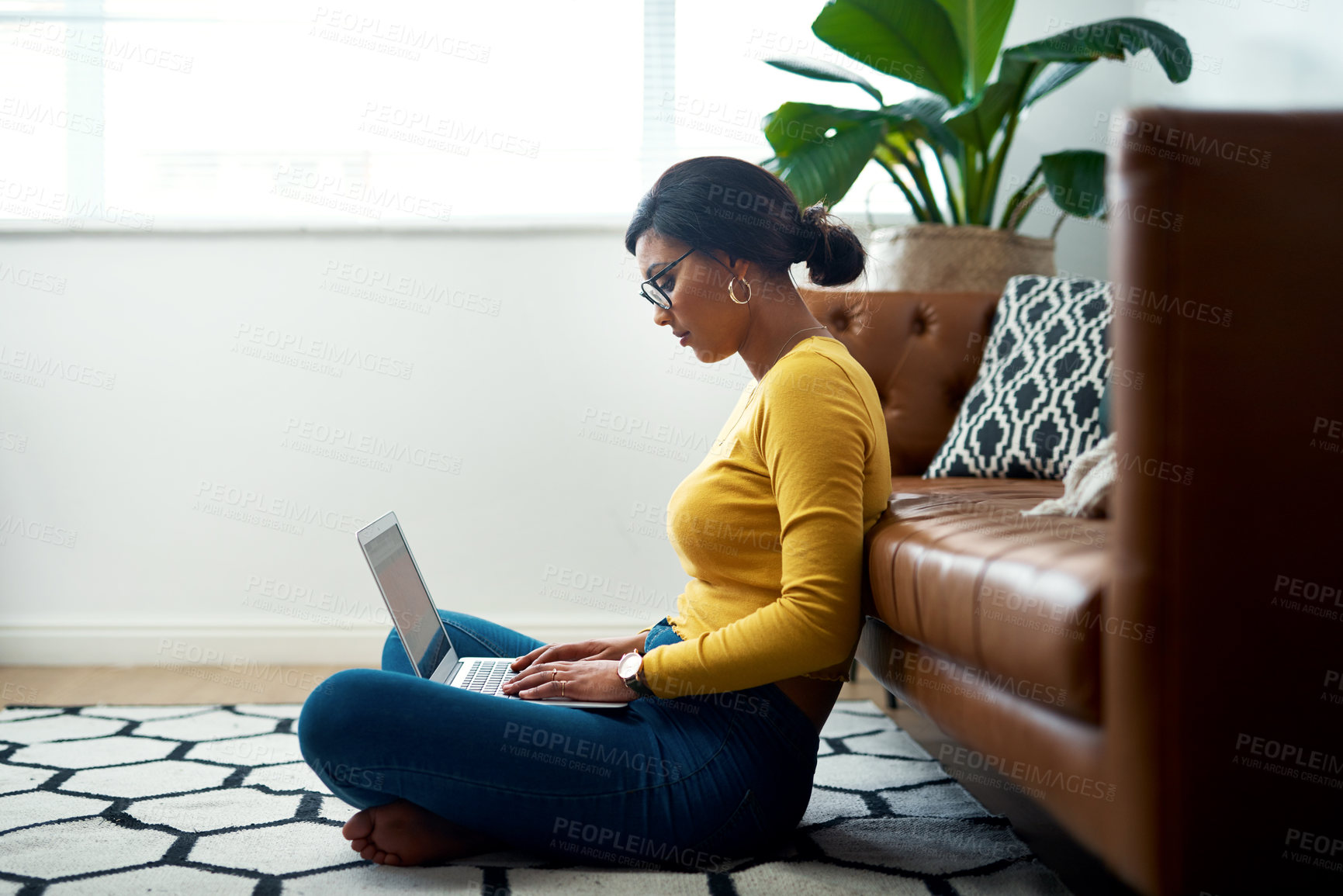 Buy stock photo Cropped shot of an attractive young woman sitting crosslegged on the floor and using her laptop at home