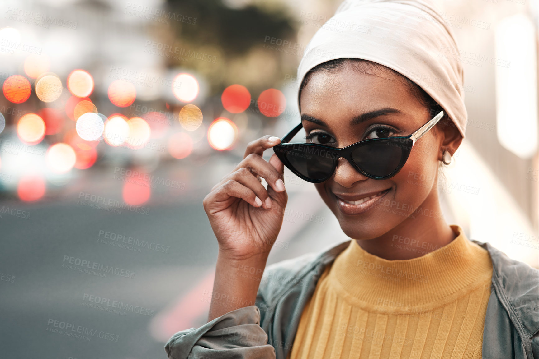 Buy stock photo Cropped shot of an attractive young woman standing alone in the city and looking alluringly over her sunglasses