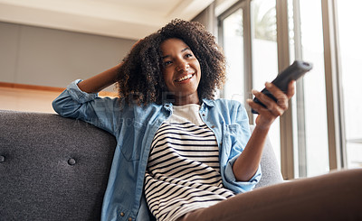 Buy stock photo Shot of a young woman holding a remote control while sitting on the sofa at home