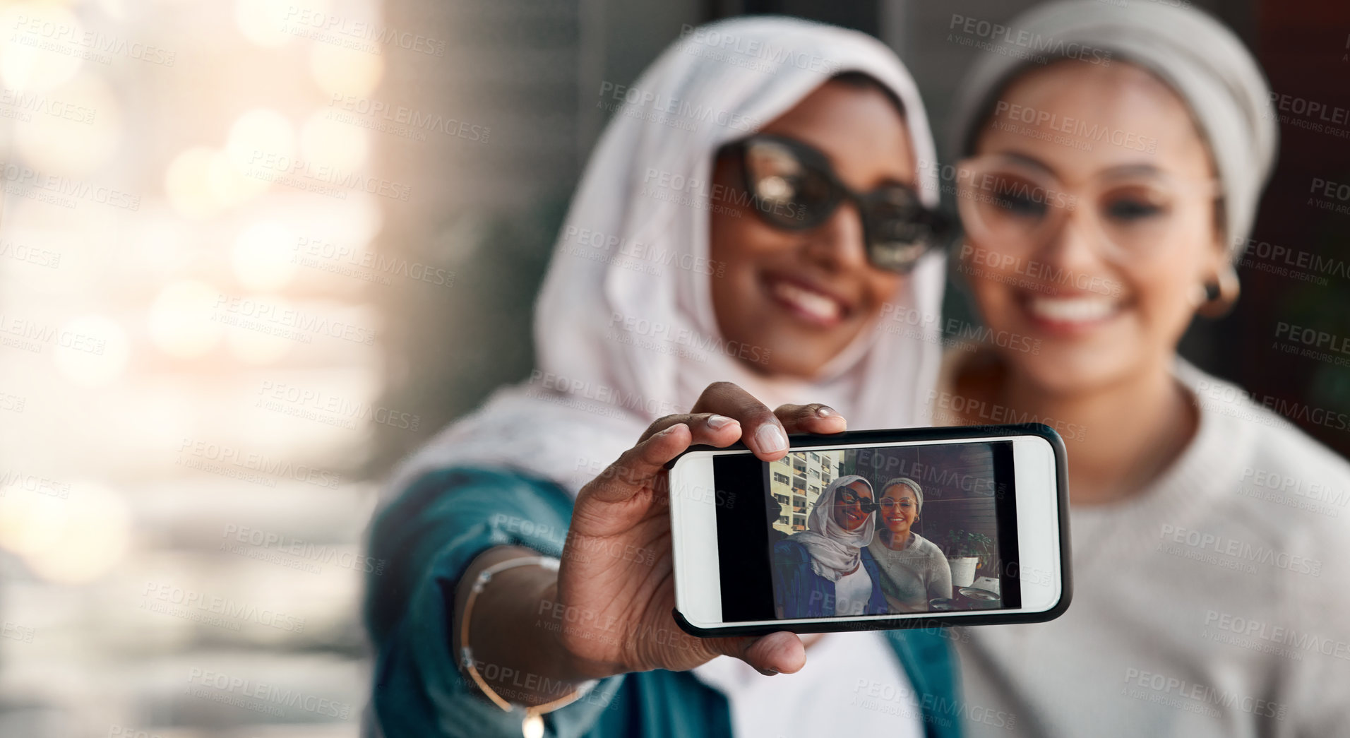 Buy stock photo Cropped shot two affectionate young girlfriends taking a selfie together at a cafe while dressed in hijab