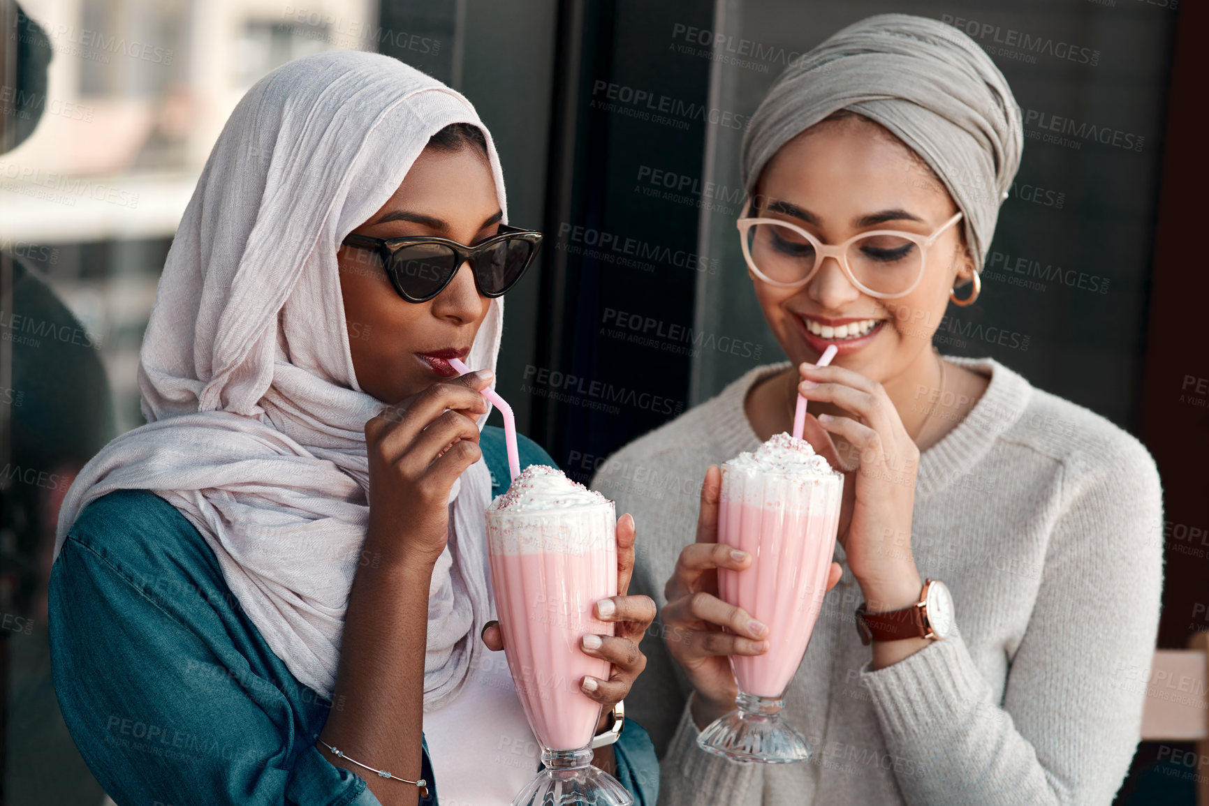 Buy stock photo Cropped shot of two affectionate young girlfriends having milkshakes together in a cafe while dressed in hijab