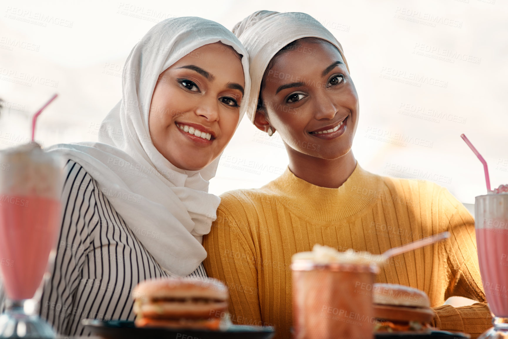 Buy stock photo Cropped portrait of two affectionate young girlfriends having a meal together at a cafe while dressed in hijab