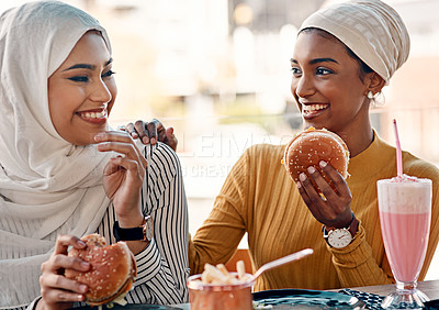 Buy stock photo Cropped shot of two affectionate young girlfriends eating burgers at a cafe while dressed in hijab