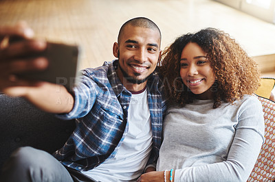 Buy stock photo Happy, romantic and in love couple taking a selfie together on phone sitting on couch. Smiling young spouses hugging while holding phone to take a picture in the living room. 