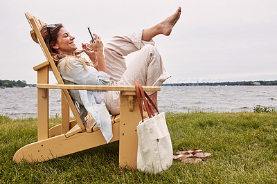 Buy stock photo Shot of an attractive young woman using a smartphone while relaxing next to the lake