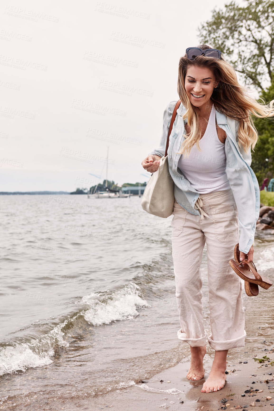 Buy stock photo Shot of a beautiful young woman going for a walk along the waters edge of a lake