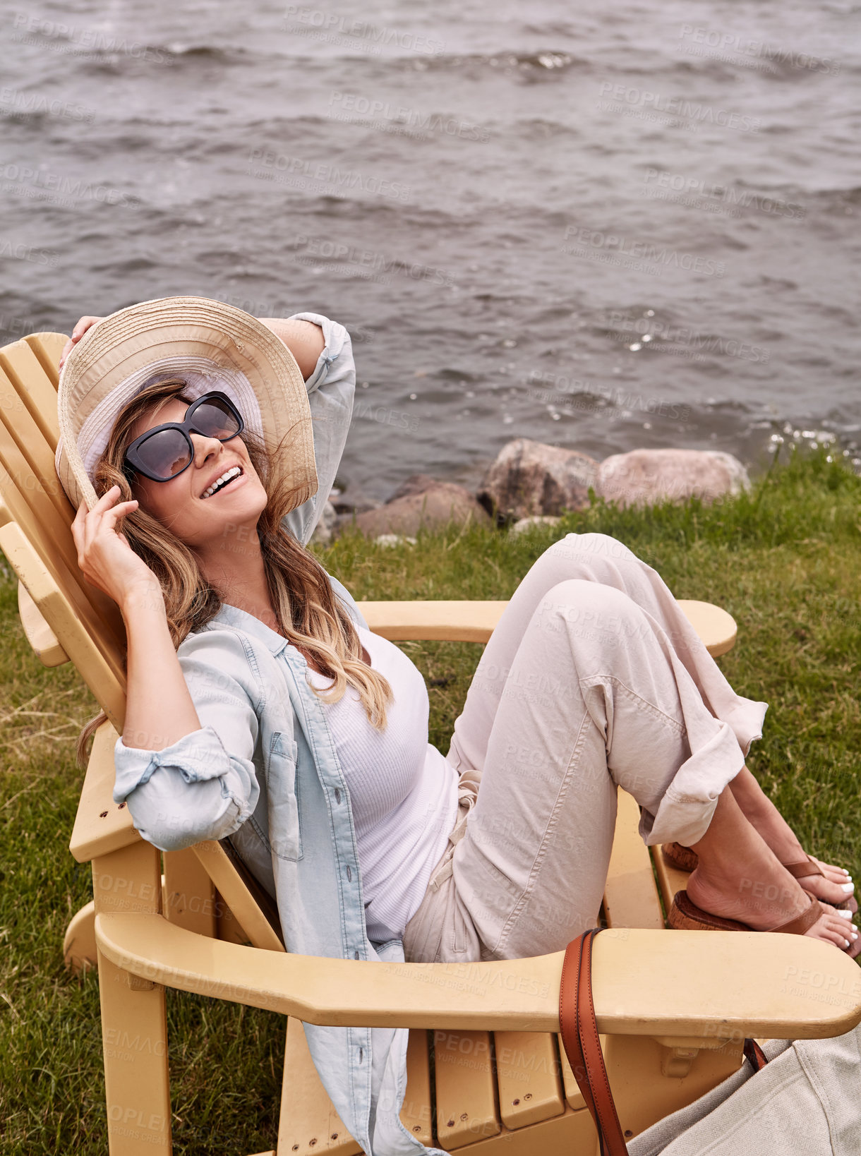 Buy stock photo Shot of a beautiful young woman relaxing on a chair next a lake