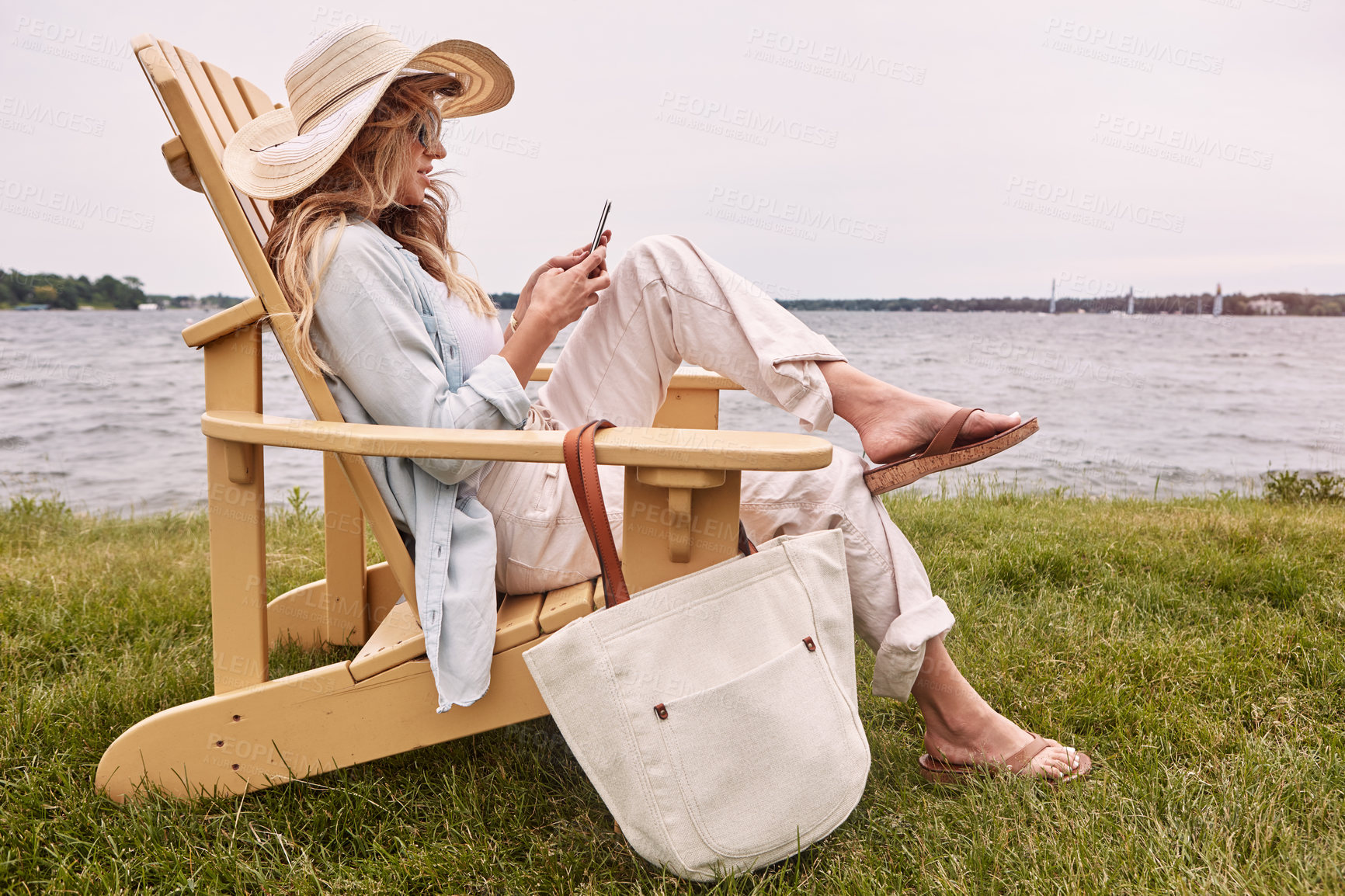 Buy stock photo Shot of an attractive young woman using a smartphone while relaxing next to the lake