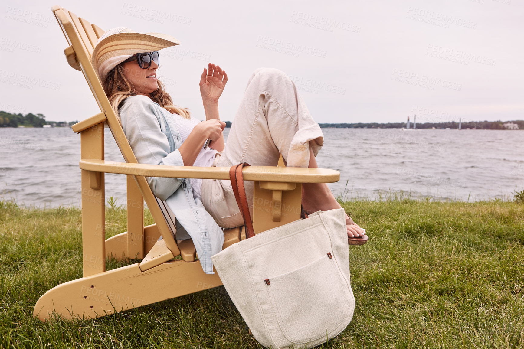 Buy stock photo Shot of a beautiful young woman relaxing on a chair next a lake