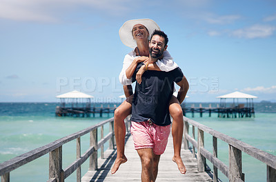 Buy stock photo Happy couple, vacation and walking on ocean boardwalk for piggy back, freedom and travel. A man and woman playing and laughing on tropical walk to relax on holiday, nature adventure or date at sea