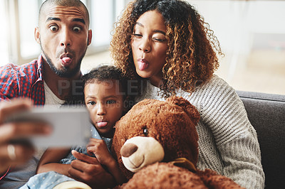 Buy stock photo Cropped shot of a happy young family of three posing for a selfie together in their living room at home
