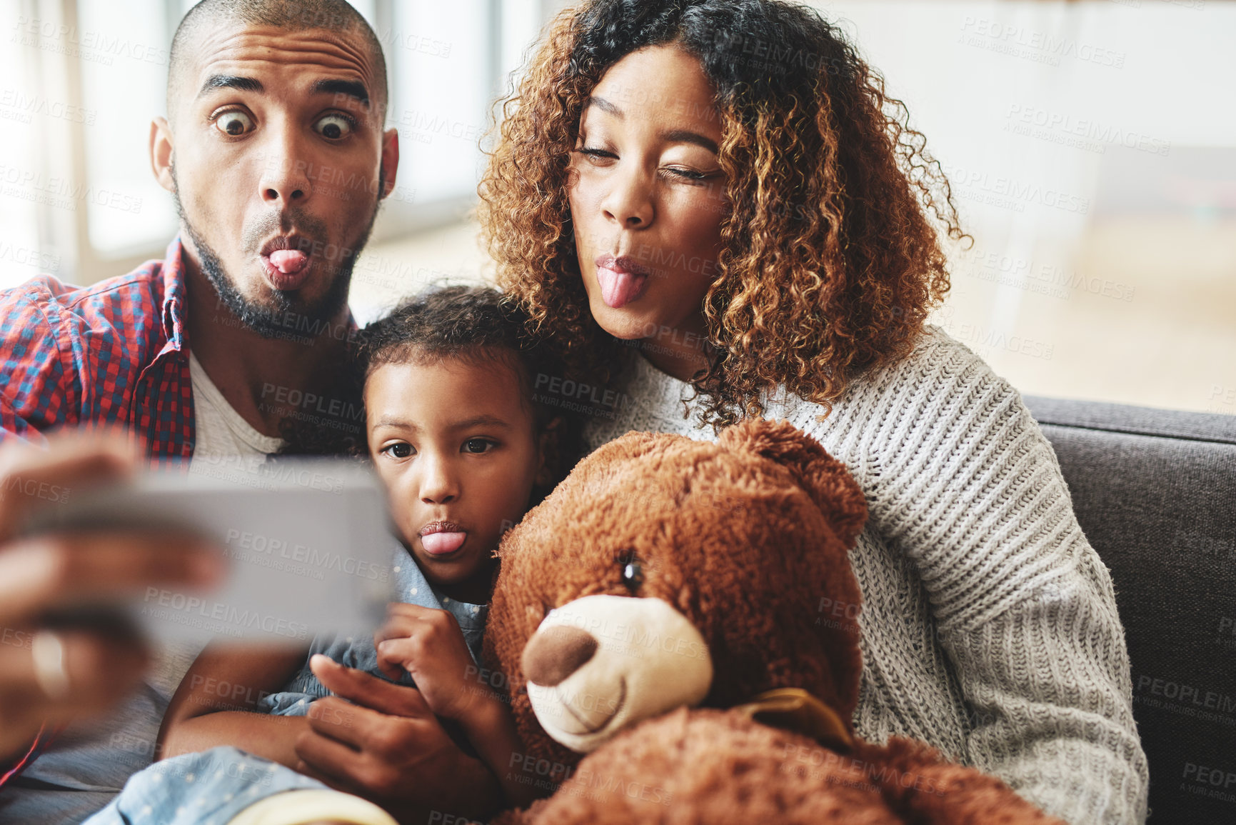 Buy stock photo Cropped shot of a happy young family of three posing for a selfie together in their living room at home