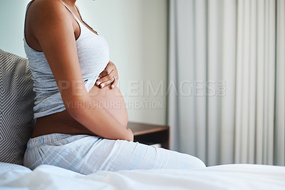 Buy stock photo Shot of an unrecognizable pregnant woman sitting on a bed and holding her belly in her bedroom at home