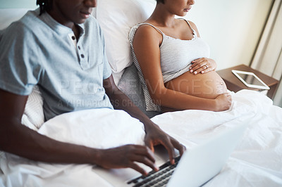 Buy stock photo Cropped shot of an unrecognizable man using a laptop while sitting bed with his pregnant wife