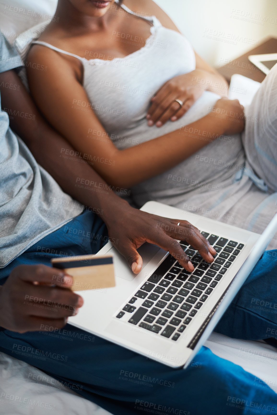Buy stock photo Cropped shot an expecting young couple doing some online shopping on a laptop while relaxing in bed together at home