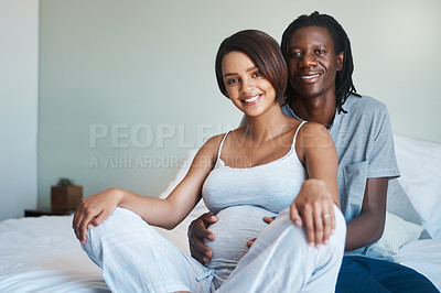 Buy stock photo Portrait of an expecting young couple relaxing and sitting on a bed together at home