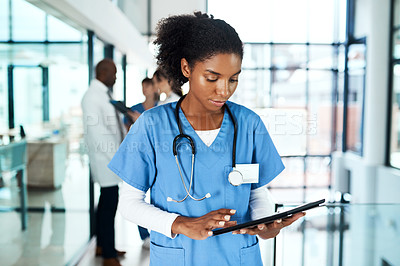 Buy stock photo Shot of a young doctor using a digital tablet in a hospital with her colleagues in the background
