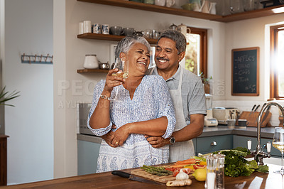 Buy stock photo Happiness, hug and old couple at kitchen counter with wine, food and cooking healthy dinner together. Smile, embrace and love, senior man and happy woman in retirement with drinks, vegetables and fun