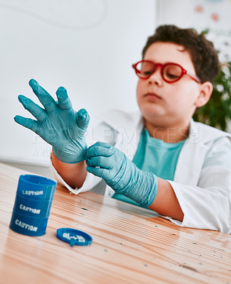 Buy stock photo Shot of an adorable young school boy putting on protective gloves in science class at school
