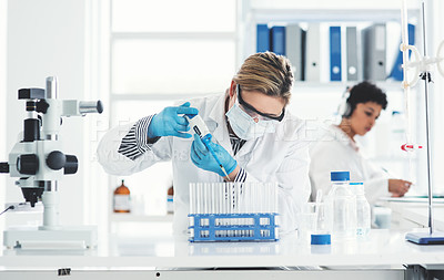 Buy stock photo Cropped shot of an attractive young female scientist transferring a liquid sample from a dropper into test tubes in a laboratory with her colleague in the background