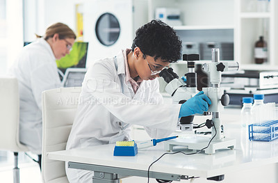 Buy stock photo Cropped shot of an attractive young female scientist looking through a microscope in a laboratory with her colleague in the background