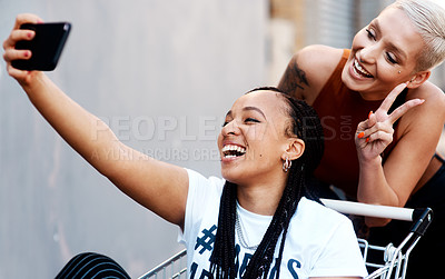Buy stock photo Cropped shot of two cheerful young girlfriends taking a selfie while playing around with a shopping cart outdoors