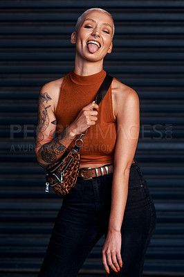 Buy stock photo Cropped shot of an attractive young woman sticking out her tongue while standing against a dark background