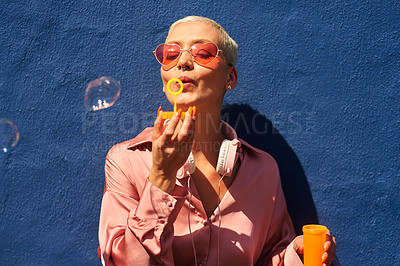 Buy stock photo Cropped shot of an attractive young woman standing against a blue wall alone and blowing bubbles while outdoors