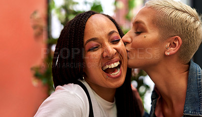 Buy stock photo Shot of an attractive young woman kissing her friend on the cheek while hanging out and having fun together outdoors
