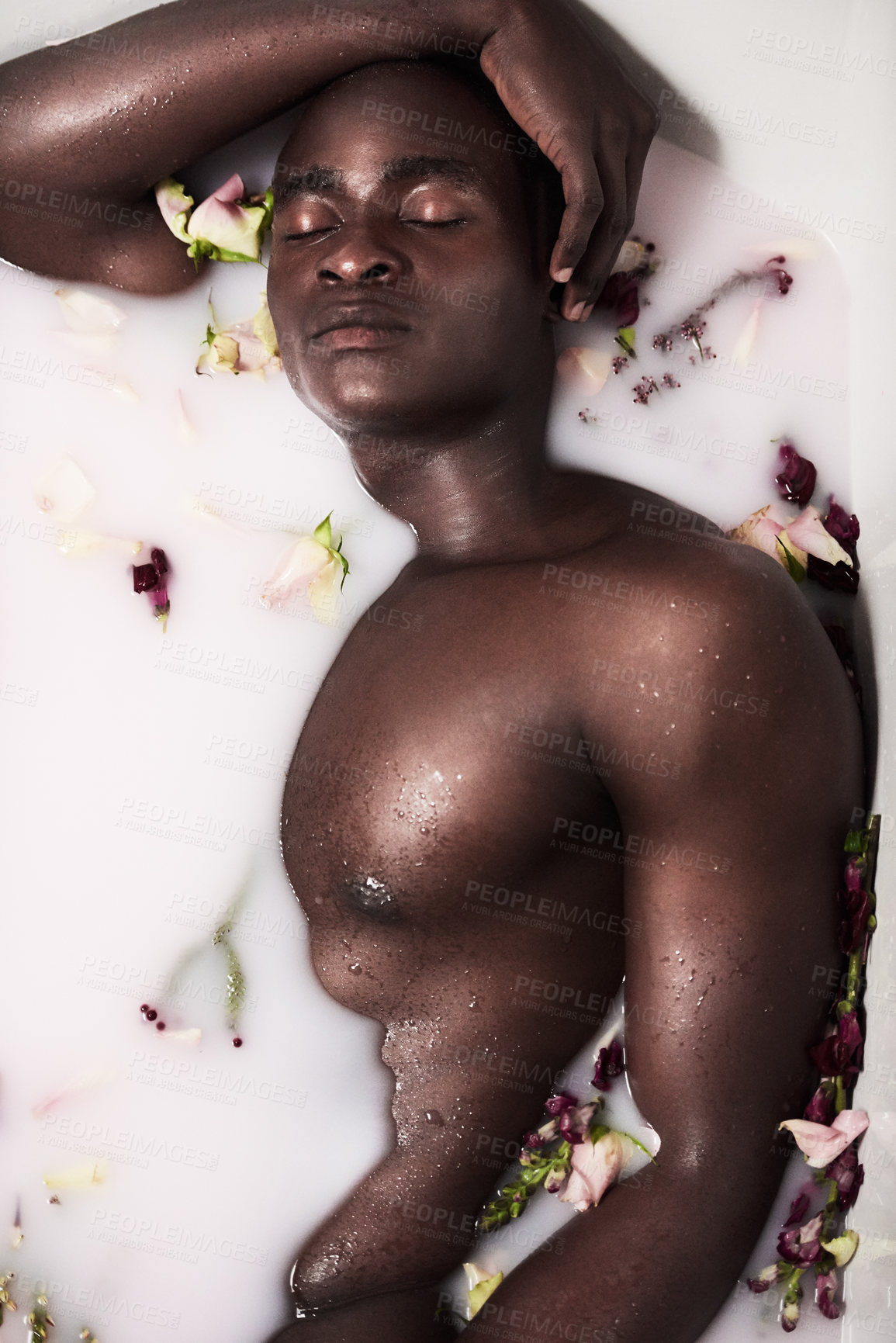 Buy stock photo Flowers, relax and black person in milk bath for smooth, clean and hydrated body care routine. Calm, spa and African  man wash in water with dairy liquid and floral plants for soft skin treatment. 