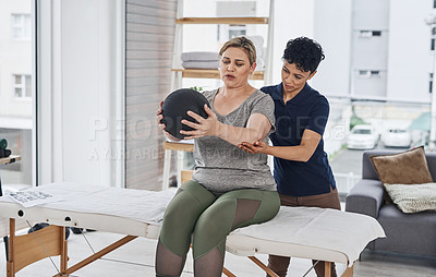 Buy stock photo Shot of a young physiotherapist helping her mature patient exercise with a medicine ball inside her office at a clinic