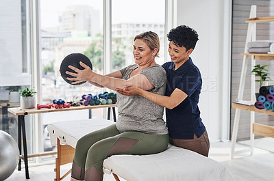 Buy stock photo Shot of a  young physiotherapist helping her mature patient exercise with a medicine ball inside her office at a clinic